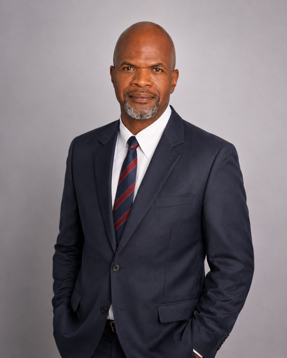 314ead2b-4b76-4d99-891a-d1e07ef7ccca | Portage Path Behavioral Health Professional head-and-shoulders portrait of a man in a navy suit, white shirt, and striped tie against a neutral gray background