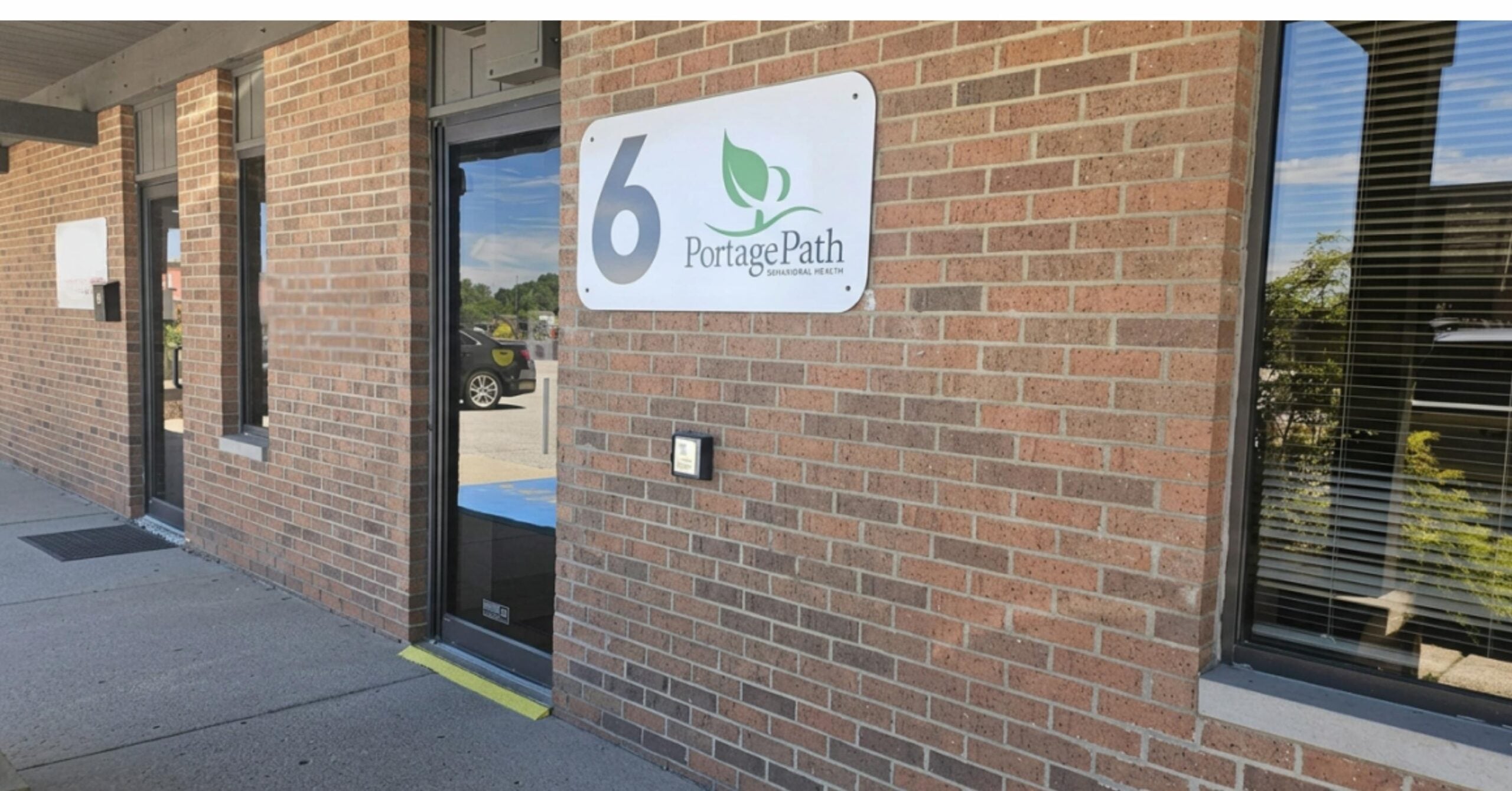 Barberton Front Door | Portage Path Behavioral Health Brick exterior with a white sign displaying the number 6 and the words portage path beside a glass door.