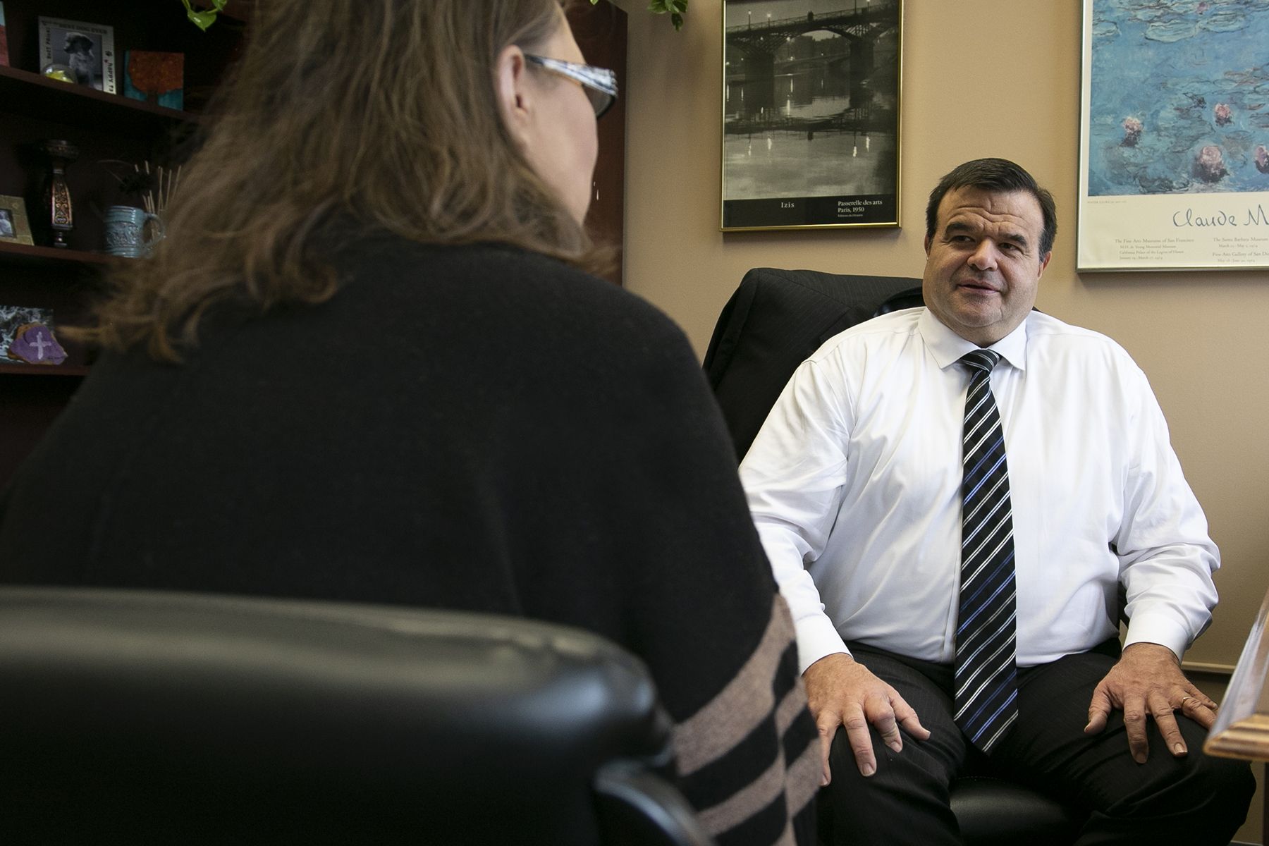 Office consultation: man in a white shirt and striped tie sits across from a client whose back is to the camera.